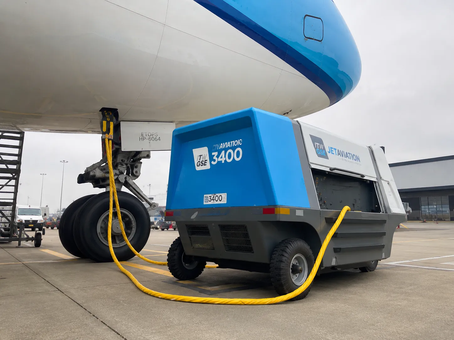 Ground Power Unit conectada a uma aeronave comercial no pátio, fornecendo energia elétrica em solo.